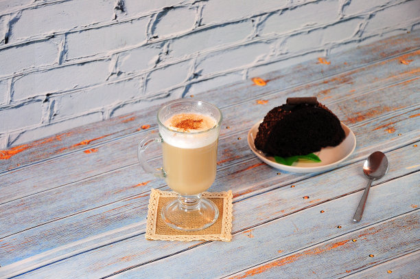 木桌上放着一块巧克力松饼，餐巾纸上放着一杯新鲜拿铁。图片下载