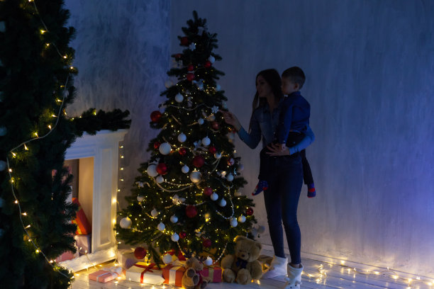 妈妈和儿子在新年前夕在圣诞树上点亮礼物花环图片下载