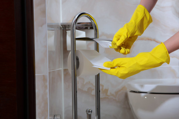 妇女的手在橡胶保护手套擦拭厕纸架。照片没有脸，只有手。浴室的清洁卫生。图片下载