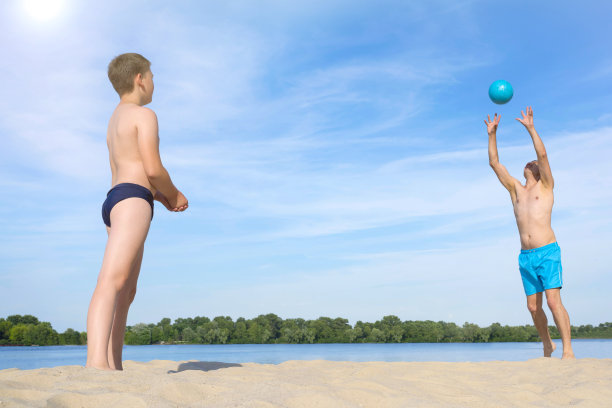 爸爸和儿子在沙滩上玩球。在阳光明媚的夏日沙滩上做运动。体育生活方式。图片下载