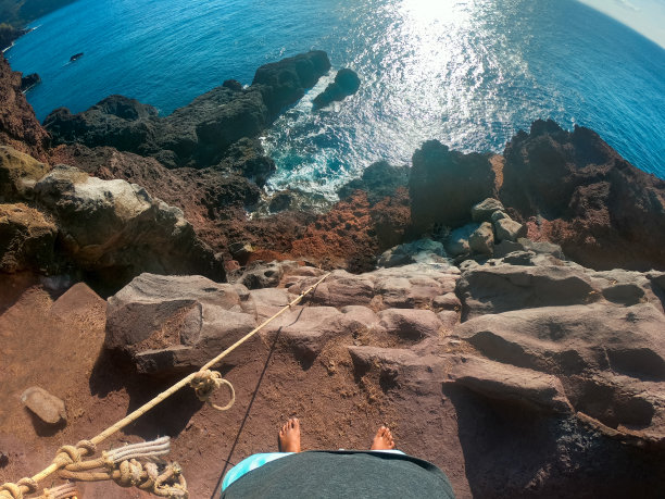 第一人称视角拍摄于夏威夷毛伊岛海岸悬崖边的岩壁上。无尽的海洋。攀爬者的腿。绳子没有固定。宽镜头。图片下载