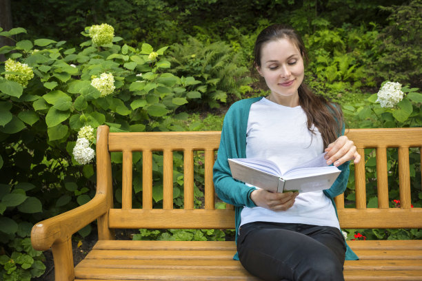 一个漂亮女孩坐在长椅上，手里拿着一本书的户外肖像。图片下载
