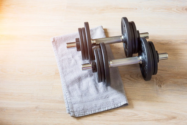 一对哑铃躺在地板上，用毛巾，在家训练。图片下载