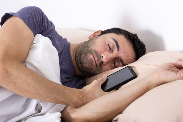 男人在床上睡觉，手里拿着移动设备图片下载