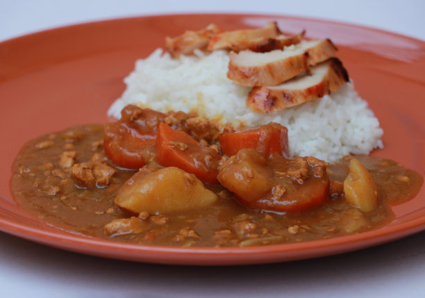 黄咖喱鸡和熟米饭在白色的地板上圆橙色的菜。图片下载