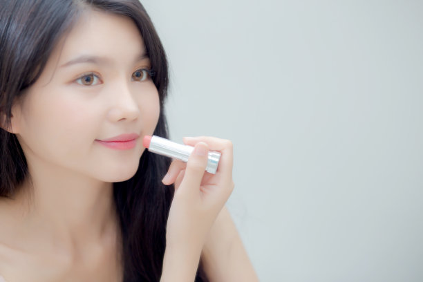 美丽的年轻亚洲女人用口红粉色的风格明亮和闪亮的嘴，美丽的女孩看镜子化妆化妆品与嘴唇优雅，时尚化妆与奢华和性感。图片下载