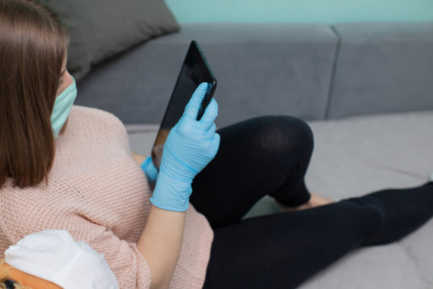 一名高中毕业生坐在床上，手里拿着药片，戴着橡胶手套和防护口罩。图片下载