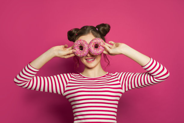 女人拿着甜甜圈在充满活力的粉红色背景，甜蜜有趣的肖像图片下载