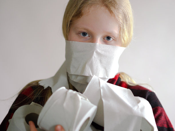 搞笑图片-由于冠状病毒的流行而被隔离。戴面具的女孩拿着一卷卫生纸在灰色背景下摆姿势。图片下载