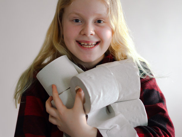 搞笑图片-由于冠状病毒的流行而被隔离。戴面具的女孩拿着一卷卫生纸在灰色背景下摆姿势。图片下载