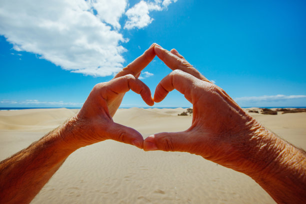 一个面目全非的人用手做了一个形状的心脏去了加那利群岛。图片下载