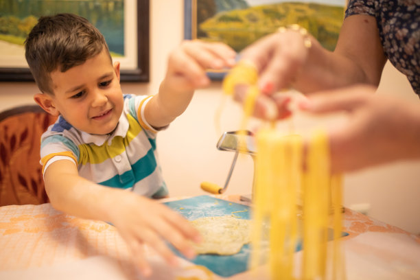 一个可爱的男孩和他的奶奶在拉伸他们自制的意大利面图片下载