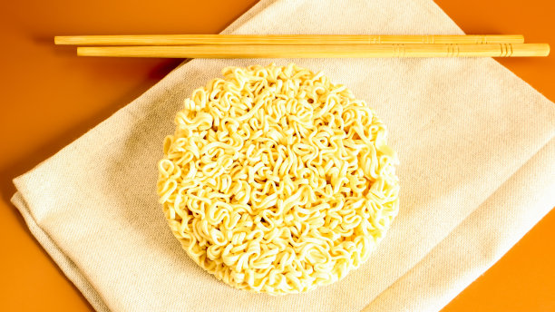 在黄色的背景上用筷子夹在毛巾上的生方便面。意大利面，为准备这是足够的倒沸水在上面，并等待几分钟。本空间图片下载