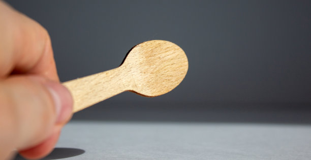 在白色背景上拿着一个木勺。美丽的温暖的阳光。图片下载