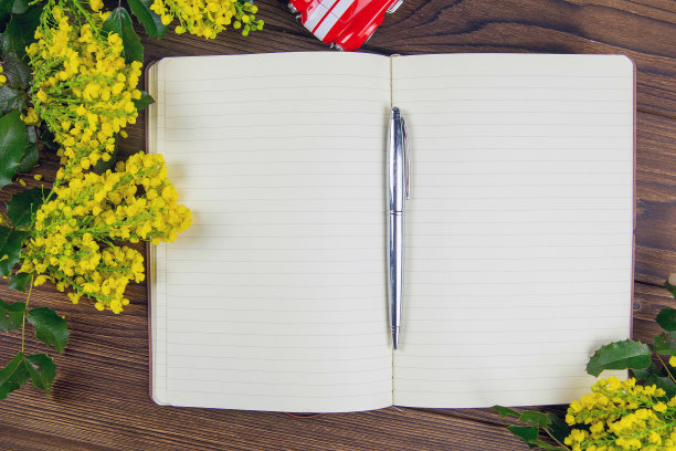 一个打开的笔记本笔记，旁边盛开着黄色的花。顶部视野与清晰的空间图片下载
