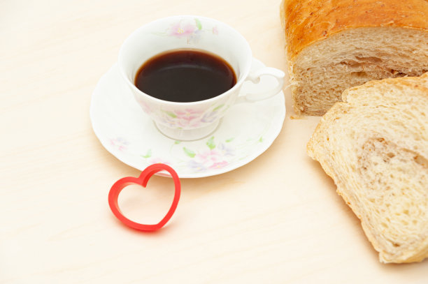 自制巴西面包切片，旁边是一杯咖啡和一个红心形状的物体。孤立在浅色木质背景上。图片下载