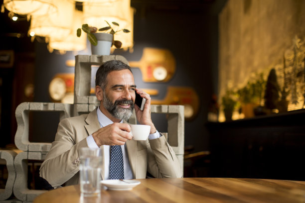 帅气成熟的商人在咖啡馆喝咖啡，用手机图片下载