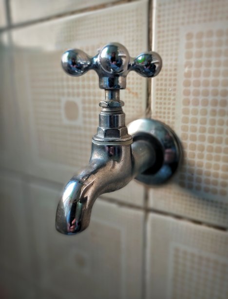 贴着瓷砖的墙上关闭的旧金属水龙头。图片下载