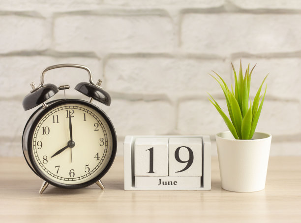 在6月19日一个木制日历旁边的闹钟桌上。夏天的一天，空白的文字。六月的日历，背景很亮。图片下载