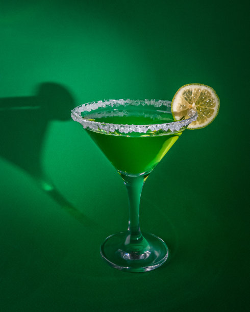马提尼杯加绿色冰沙和青柠片。玻璃杯的边缘加了糖。在纯绿色的背景上。强光，清晰的阴影。特写镜头。文本。图片下载