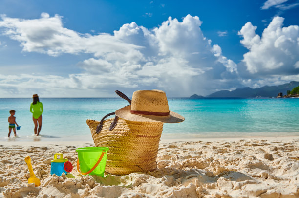 蹒跚学步的男孩和妈妈在海滩上。沙滩包和玩具。图片下载