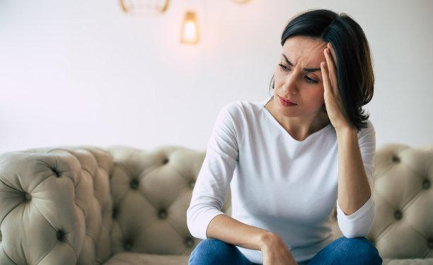 身体的痛苦。一个年轻女子的特写照片，她是坐在沙发上，触摸她的头，而遭受头痛。图片下载