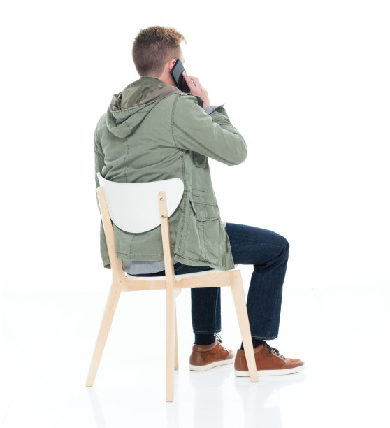 白人少年坐在白色背景前，穿着夹克，使用手机图片下载