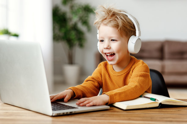 快乐的小男孩戴着耳机使用笔记本电脑图片下载