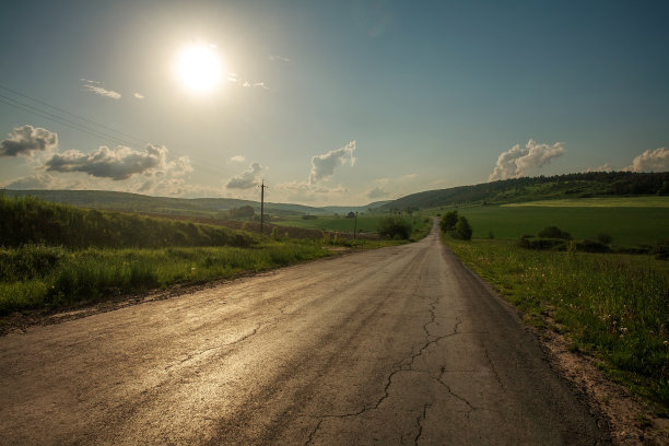 在山峦和天空的背景下，乡间的道路在破旧的柏油路中间图片下载
