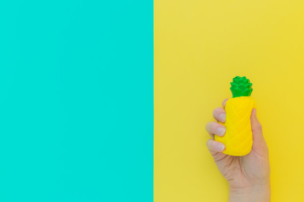 平铺抗压力玩具压扁黄色菠萝与绿色的叶子在手里。明亮的蓝色背景。压缩的，柔软的，可压缩的物品来缓解压力，问题，焦虑，担忧。夏天的概念图片下载