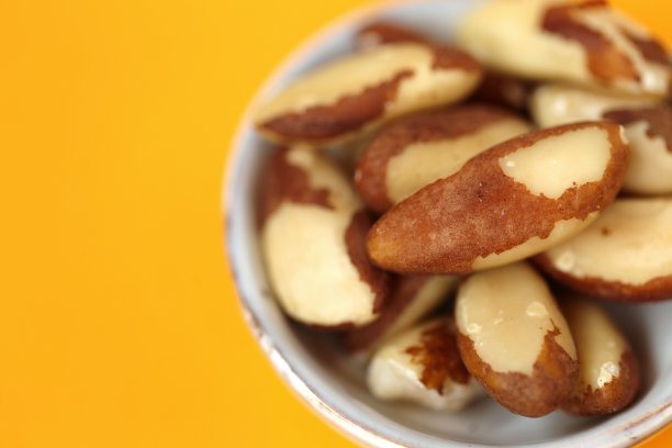 巴西坚果在陶瓷灰色杯上明亮的橙色背景。健康食品和零食。健康的脂肪成分。素食和纯素食品。酮饮食。副本的空间。图片下载