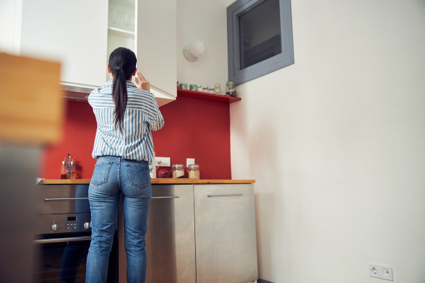 穿着衬衫的年轻女孩在厨房的橱柜里寻找食品杂货图片下载