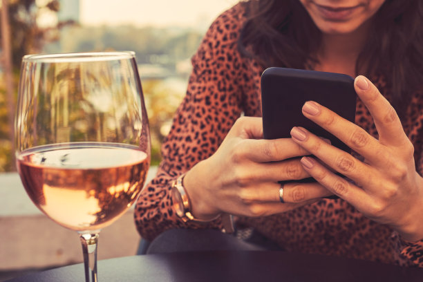 漂亮女人在户外用手机喝酒的照片。专注于手中。图片下载