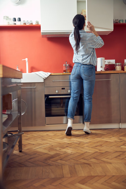 穿着衬衫的年轻女孩从厨房的橱柜里拿东西图片下载