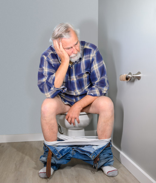 年长的白人男子坐在马桶上复杂地看着一个空的卫生纸卷。图片下载