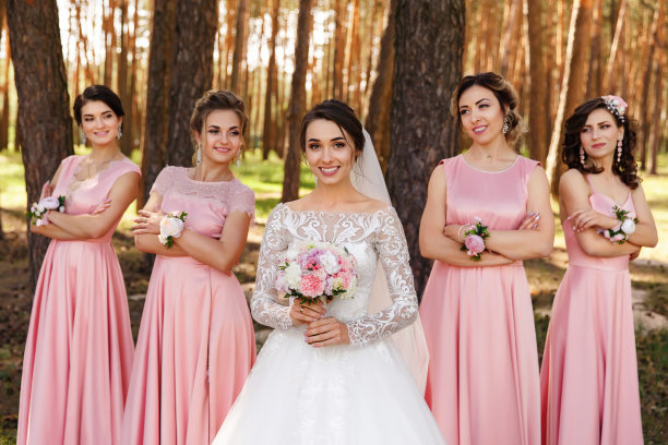 身穿粉色礼服的伴娘和身穿白色婚纱的新娘捧着一束鲜花，看着镜头图片下载