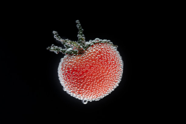 红樱桃番茄，绿叶覆盖着气泡矿泉水。工作室拍摄特写。水柱上黑色背景上的红色成熟蔬菜的水平照片图片下载