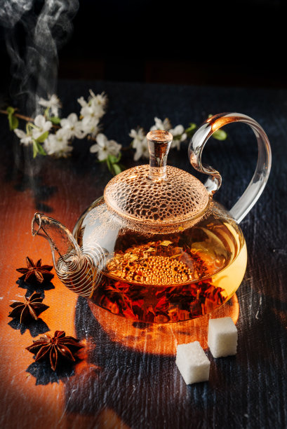 透明玻璃茶壶在黑暗的背景与糖块和八角。图片下载