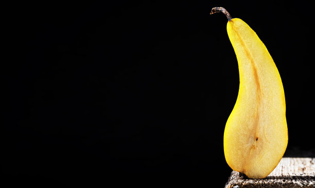 半熟的梨——天然的甜品。半个水果架在一张老式桌子的边缘，明亮的阳光，深色的背景和文本复制空间。特写镜头。图片下载