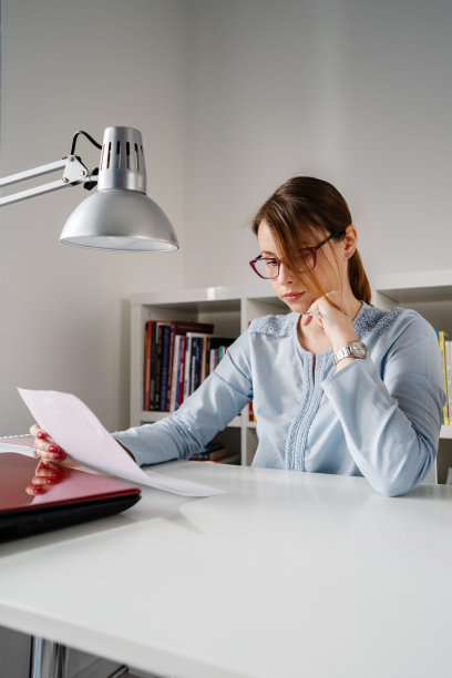 侧面的观点，年轻的白人妇女女性女孩坐在桌子在办公室工作拿着文件阅读分析研究被解雇或坏的报告在危机经济衰退的一天图片下载