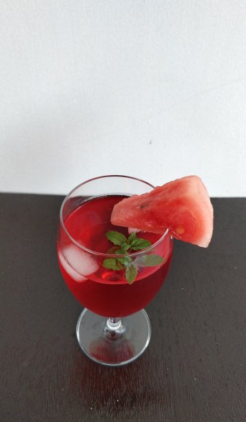 冰镇的红色冷饮，盛于红酒杯中，加冰和薄荷。用一块三角形的西瓜片装饰，简单地把它挤在杯沿上。图片下载