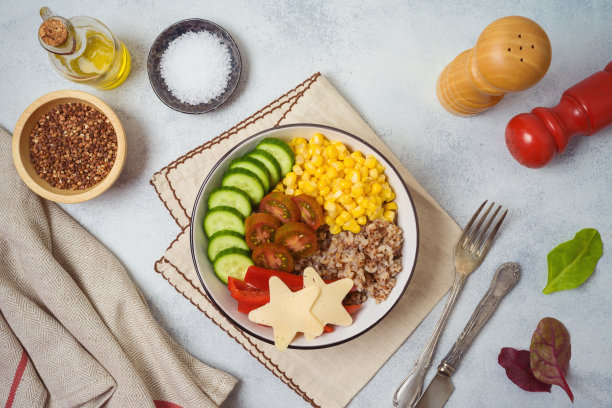 在质朴的餐桌上放着装有荞麦、番茄、黄瓜、红甜椒和玉米的佛碗。从上面俯视图片下载