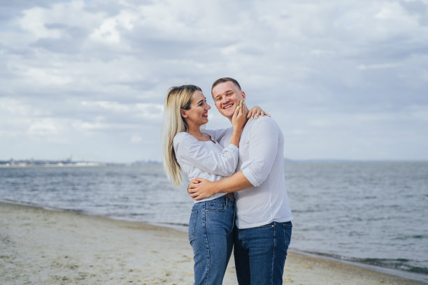 迷人的年轻女子拥抱的男朋友在海上的背景。户外照片，幸福的夫妇站在海边。暑假的概念。休闲风格。快乐的在一起。户外拍摄图片下载