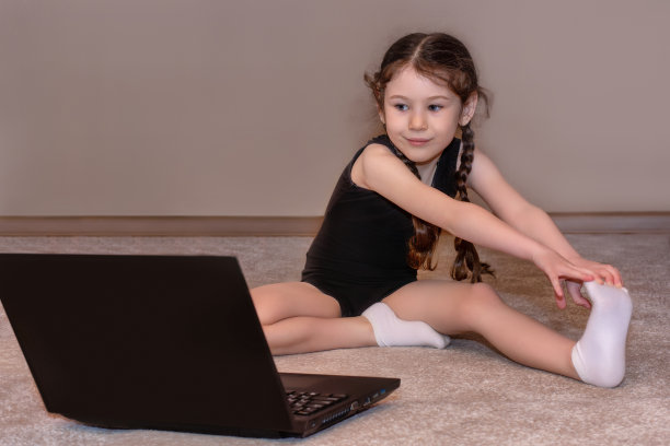 漂亮的小女孩在家里做运动健身，看着笔记本电脑的屏幕。与私人教练进行远程训练。在冠状病毒隔离期间，待在家里，保持社交距离，自我隔离图片下载