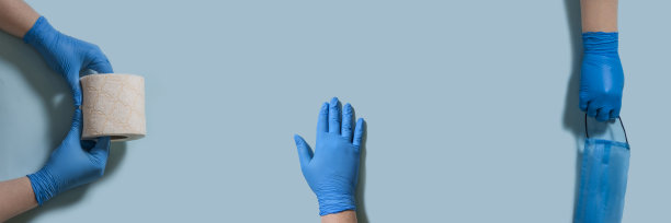 女性双手戴着蓝色无菌橡胶手套，手上拿着一个保护性的外科口罩和蓝色背景的卫生纸。清洁的概念，病毒防护，阻止冠状病毒。图片下载