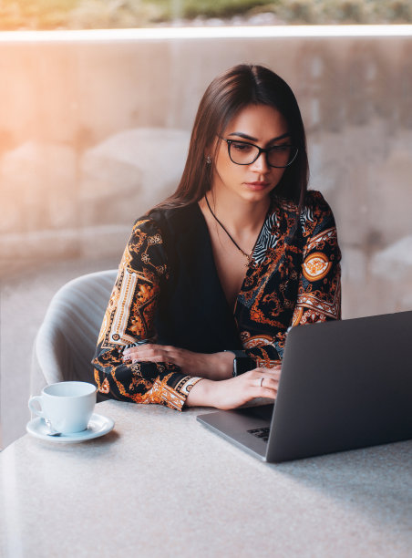 戴眼镜的年轻女商人在喝咖啡休息时。使用笔记本电脑。图片下载