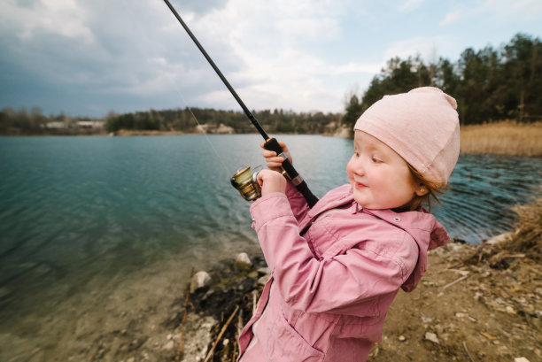 孤独快乐的小孩从海滩、湖泊或池塘钓鱼与文字空间。小女孩抓了一条鱼。孩子们在周末钓鱼时拉杆的照片。图片下载