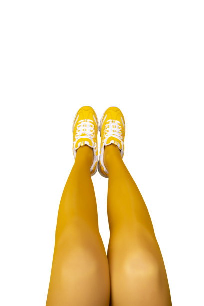 新的黄色女运动鞋在长女人的腿在黄色紧身衣孤立在白色的背景。图片下载