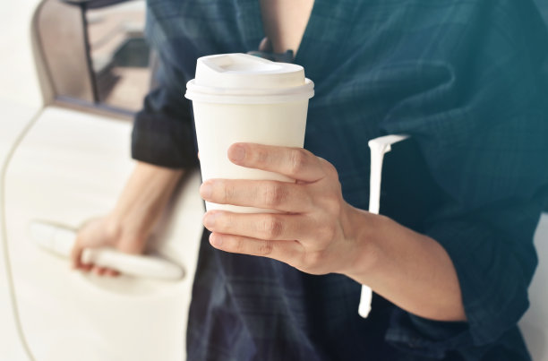 一个女人拿着一杯咖啡站在她的车前。图片下载