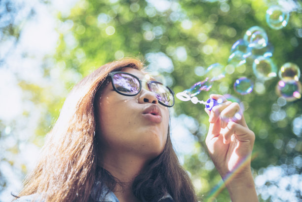 可爱的快乐可爱的女孩顽皮的泡沫泡沫在绿色的操场在夏天的户外。快乐的女孩在公园里快乐的时光。泡泡吹肥皂好玩的自然公园。图片下载